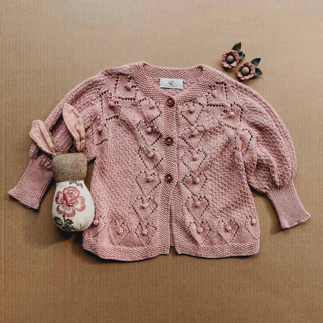 Blush-beige knit cardigan with button front and textured diamond pattern, long sleeves.