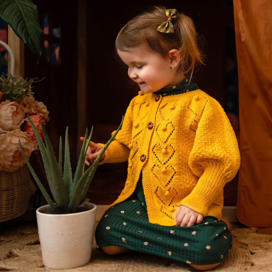 Light mustard knit cardigan with button front and diamond pattern, long sleeves.