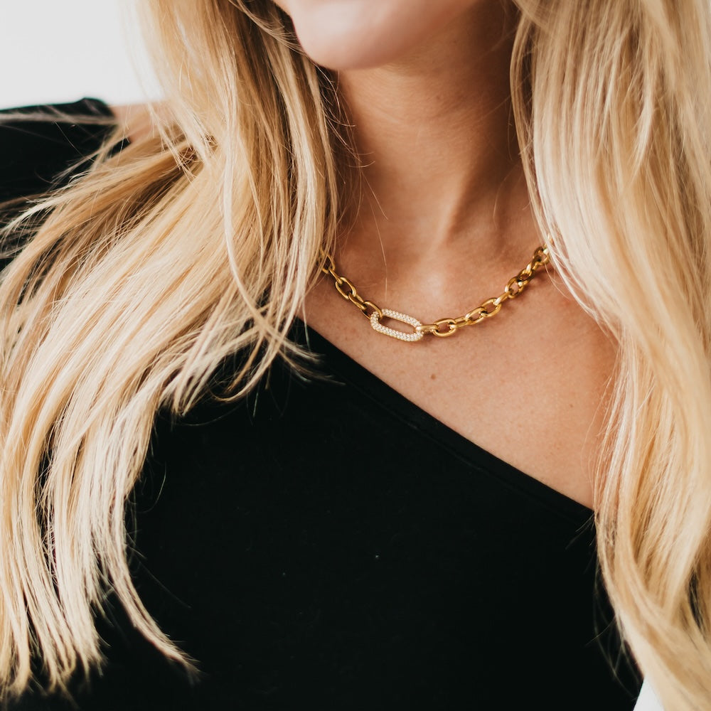 Gold tone chain necklace with oval link design and small sparkling charm at front.