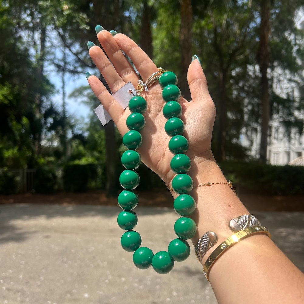 Green beaded bag charm/necklace with gold clasp and round links, held in hand