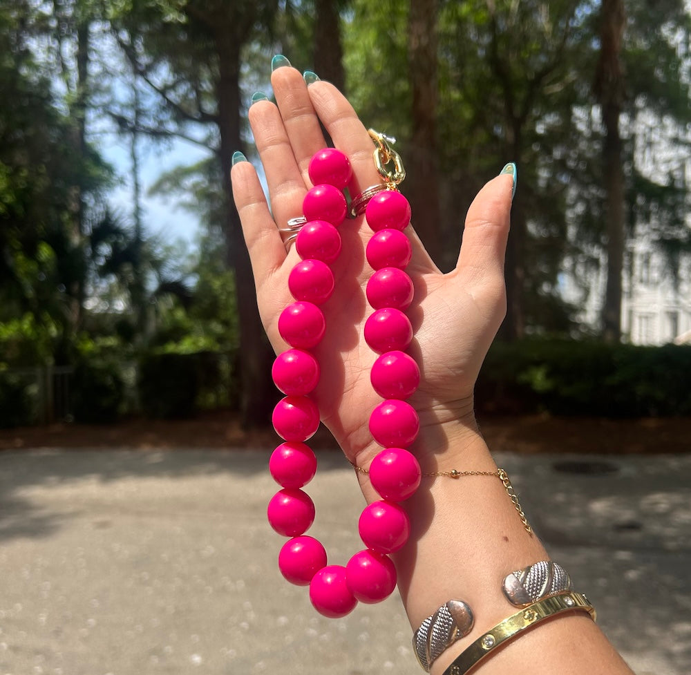 Hot pink beaded bag charm/necklace with gold clasp and ring, held in hand