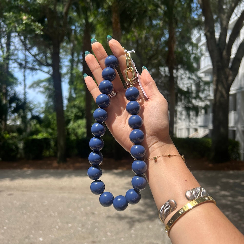 Navy beaded bag charm/necklace with gold clasp and ring, shown on hand
