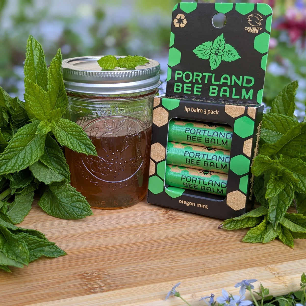 Lip balm jar and Portland Bee Balm pack with green mint leaves on a wooden surface