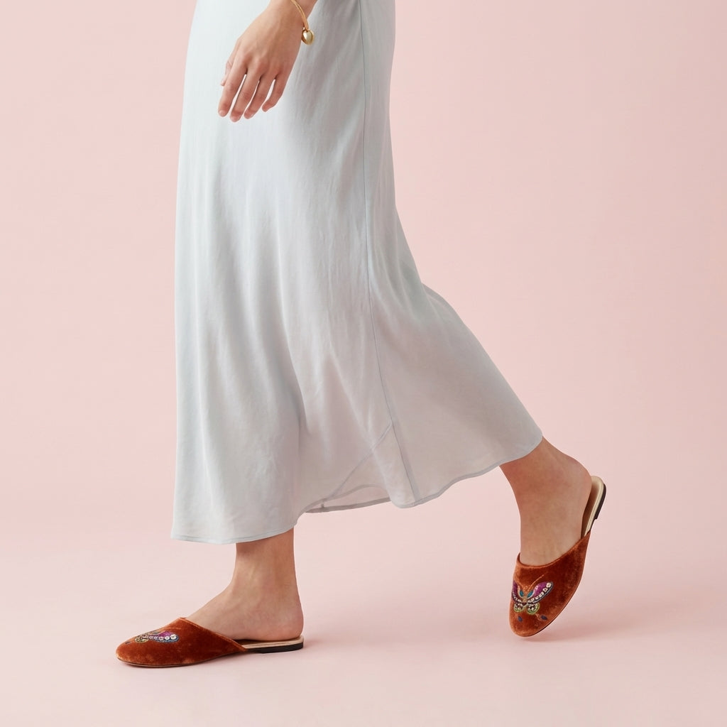 Burnt orange velvet mule slippers with embroidered butterfly, worn on feet