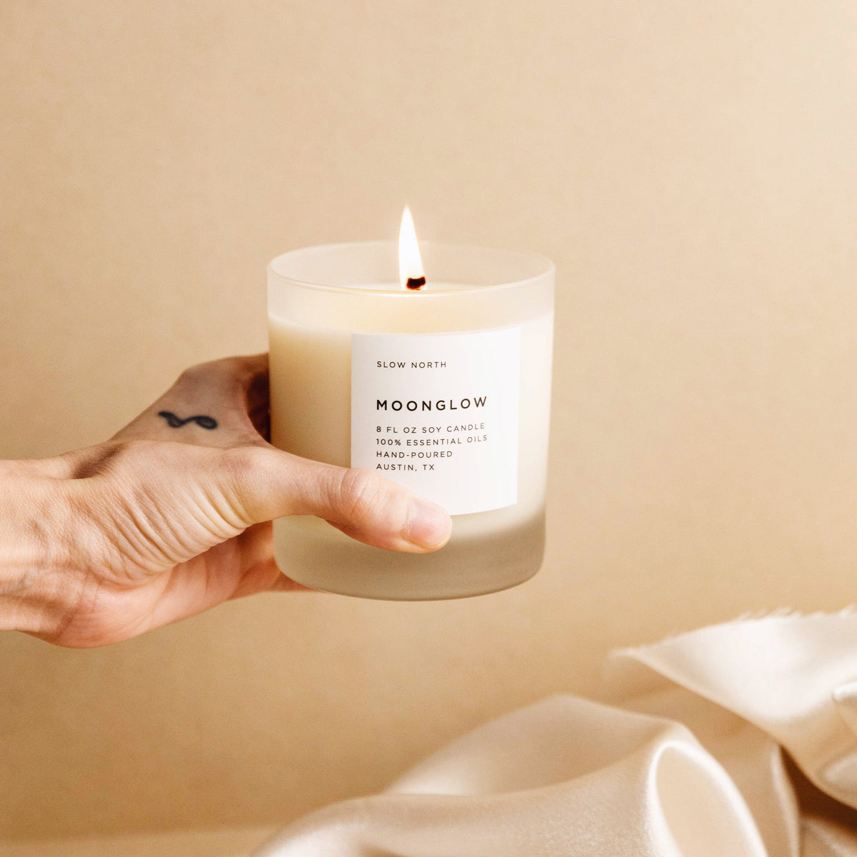 Hand holding a lit Moonglow candle in a frosted glass jar.