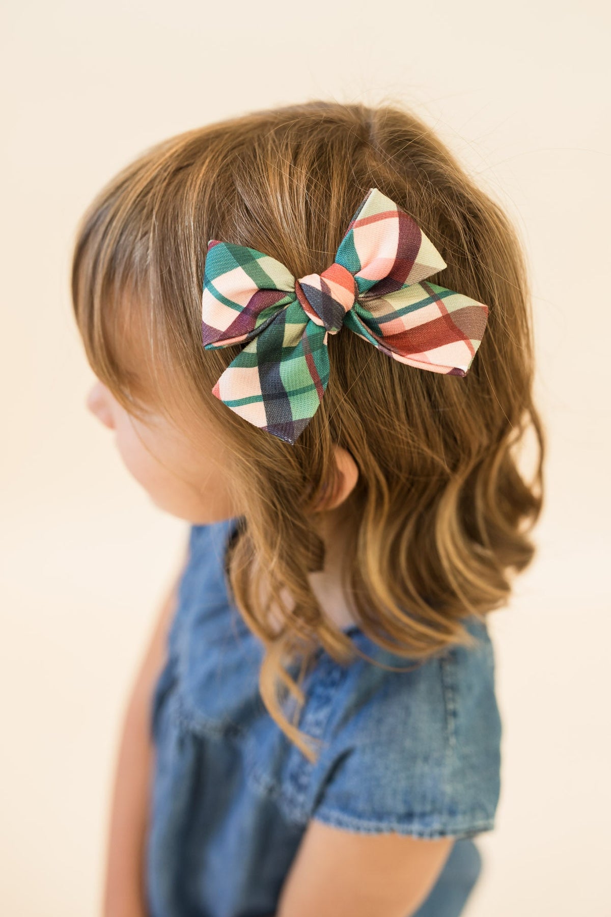 Plaid hair bow clipped to light brown hair, green red cream multi-color checks