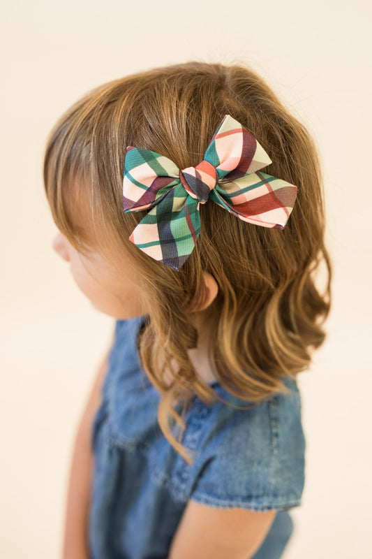 Plaid hair bow clipped to light brown hair, green red cream multi-color checks