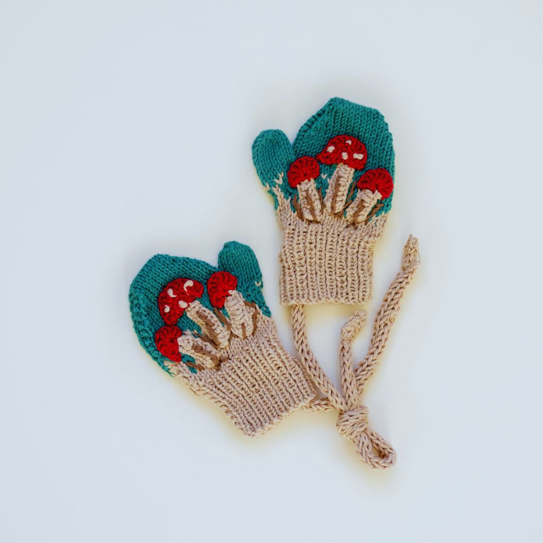 Green knit mittens with embroidered red mushrooms and cream cuffs, tie strings