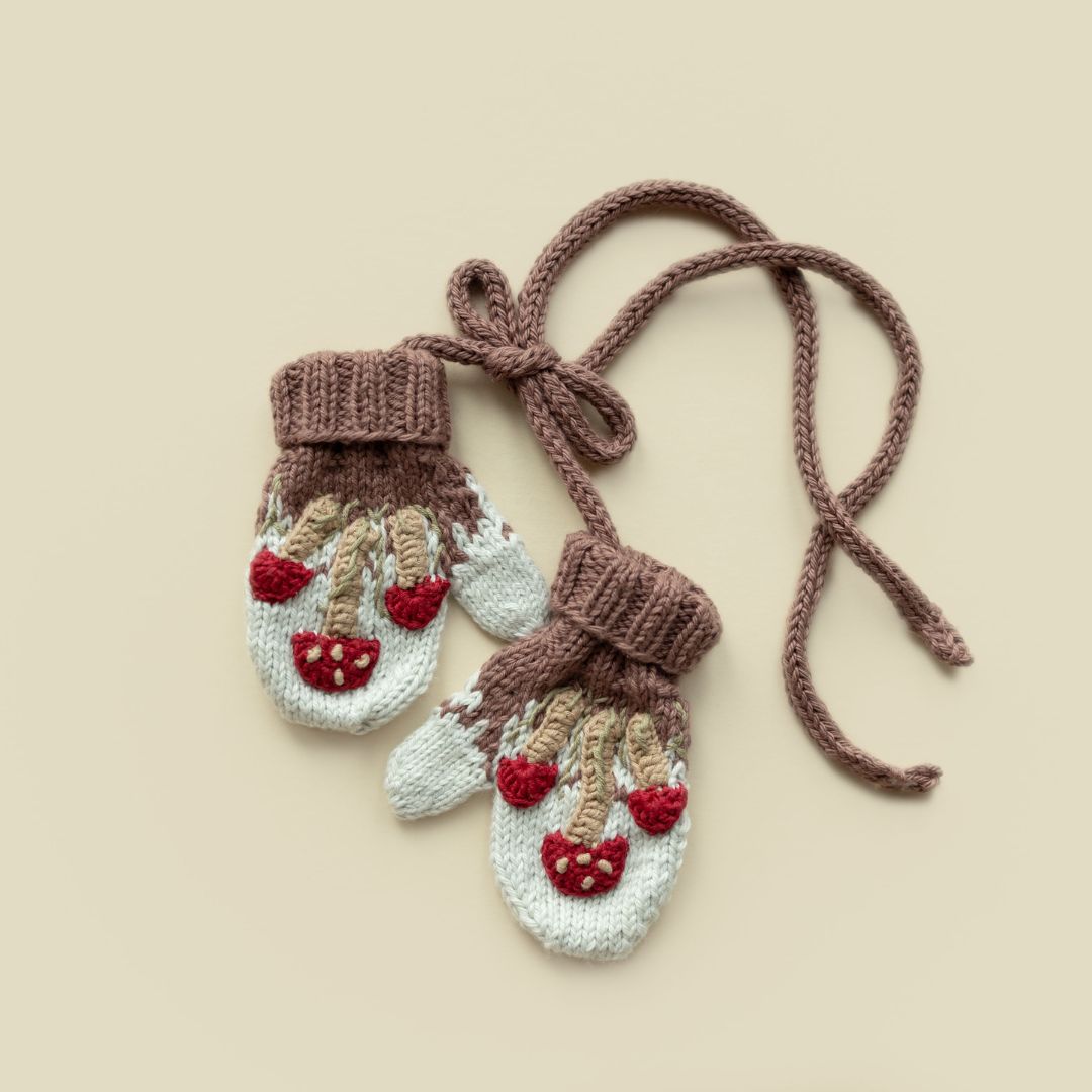 Light gray knit mittens with red mushroom embroidery and brown tie strings