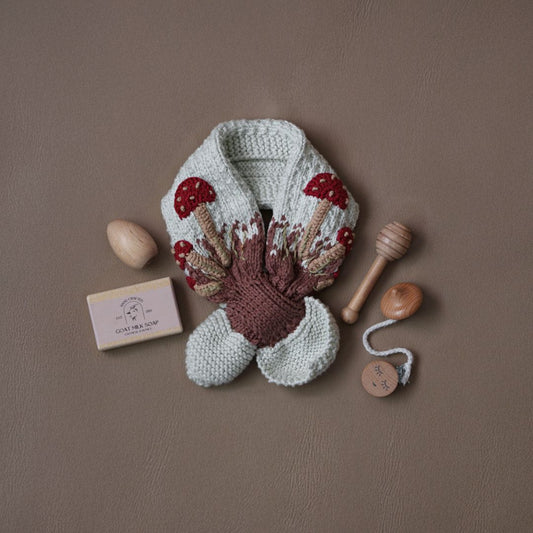 Knit mushroom neck scarf flat lay with light gray fabric and red mushroom caps