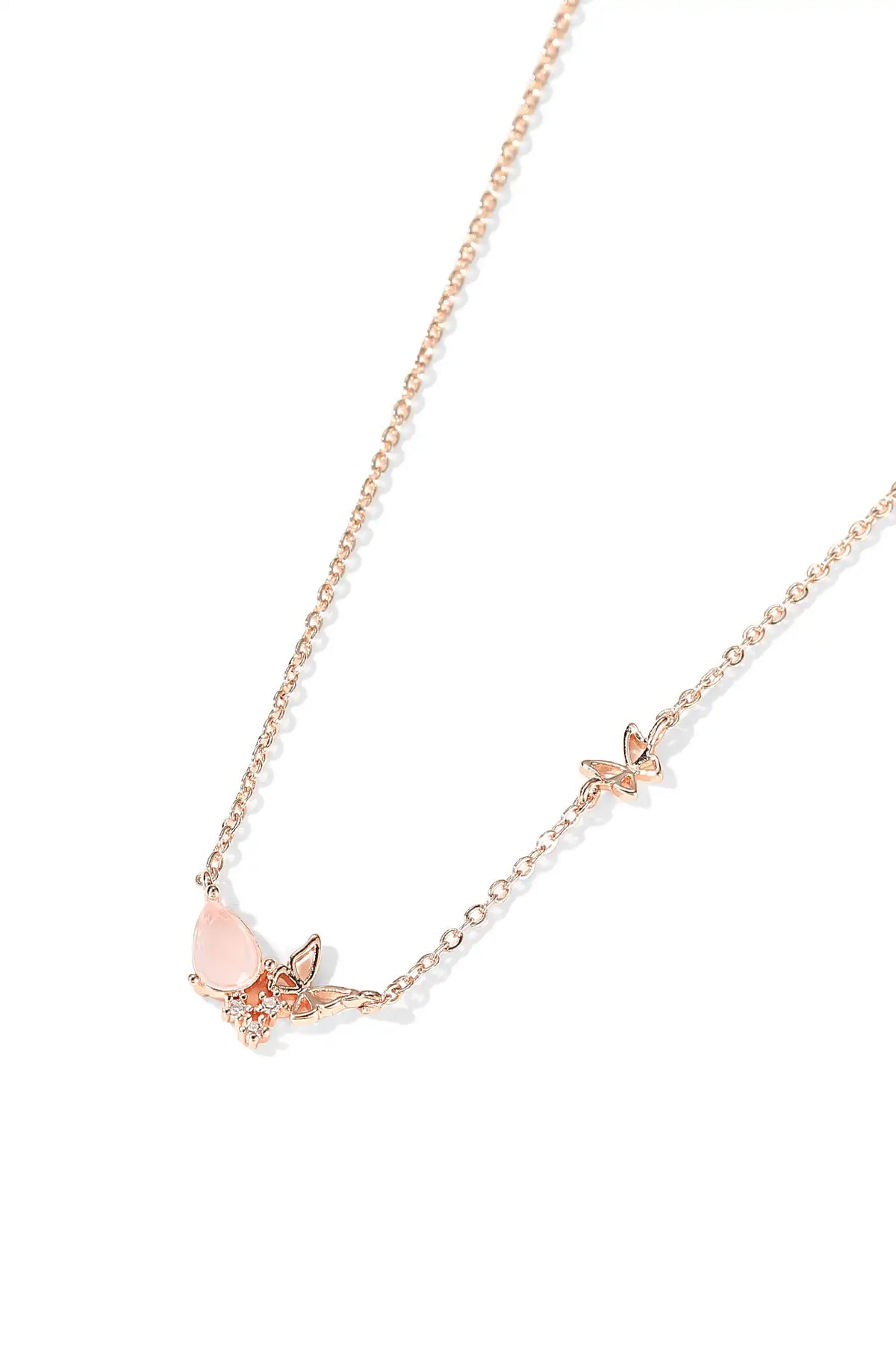 Rose gold-tone necklace with a pale pink teardrop pendant and small butterfly charms