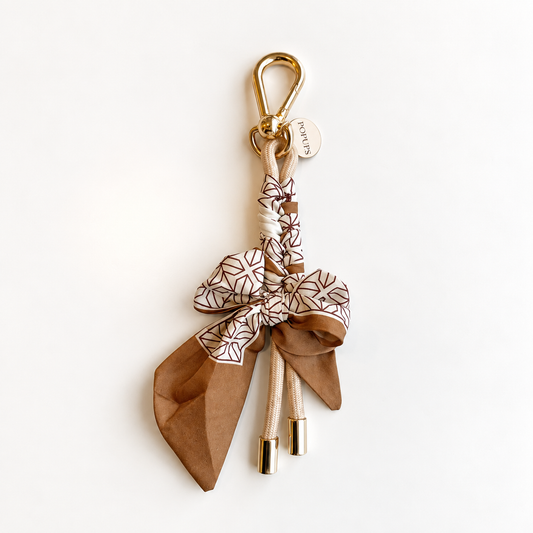 Tan patterned scarf keychain with gold clasp and dangling metal charms