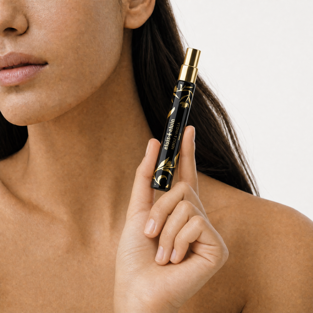 Neroli & Vanilla parfum roller bottle held by hand near neck, dark glass and gold cap