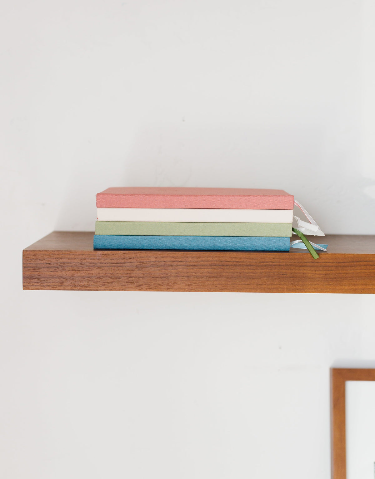 Stacked linen-look notebooks with ribbon ties in pink, cream, and blue
