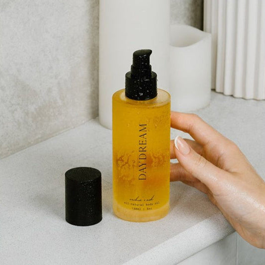 Amber body oil bottle with black pump and small cap on counter.