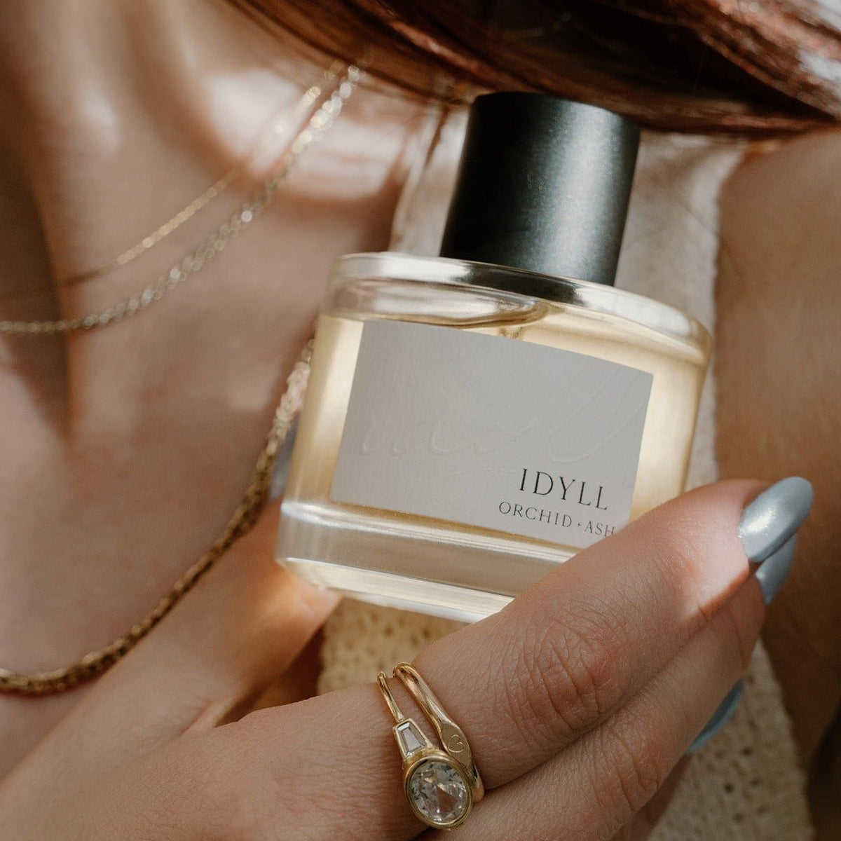 IDYLL perfume bottle held in hand with black cap and white label