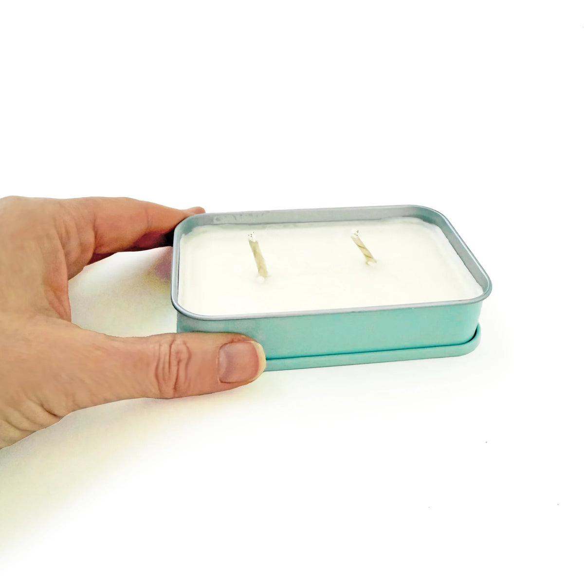 Soy wax candle in teal tin held in hand, three wicks visible
