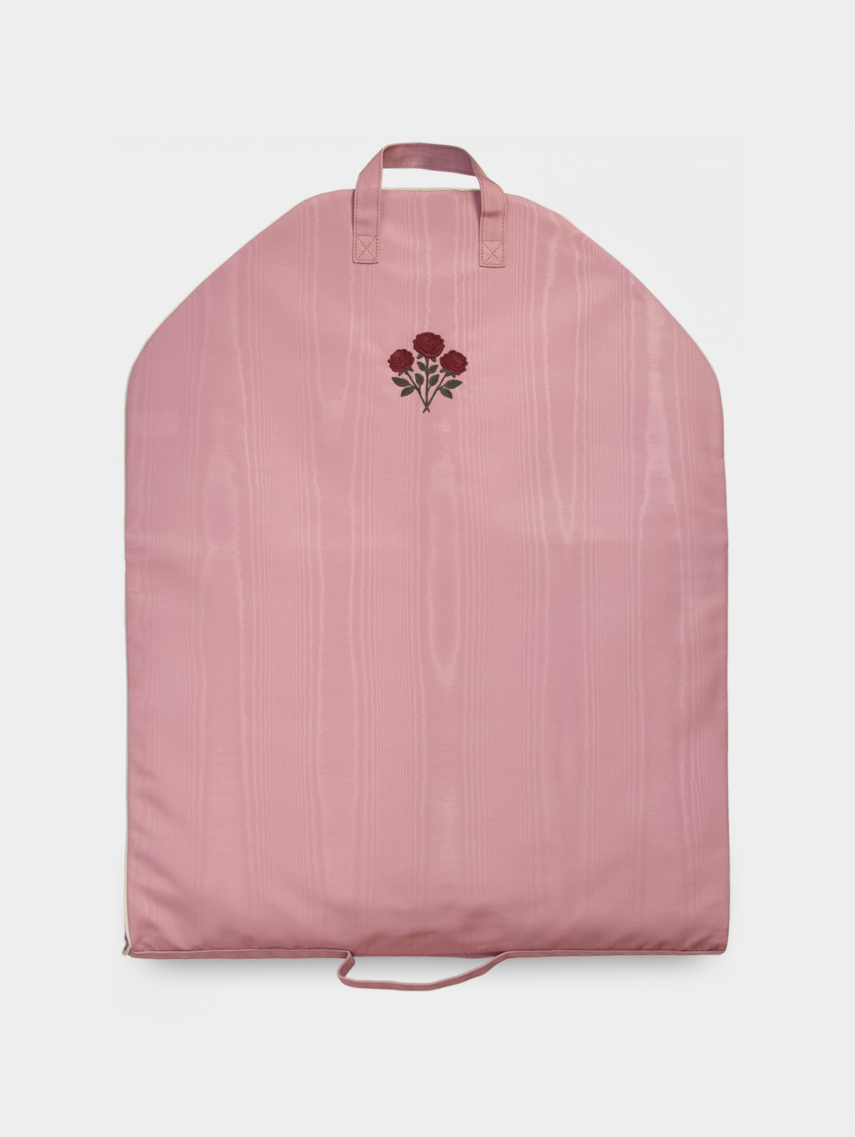 Pink garment bag with top handles, vertical stitched panels, and floral embroidery