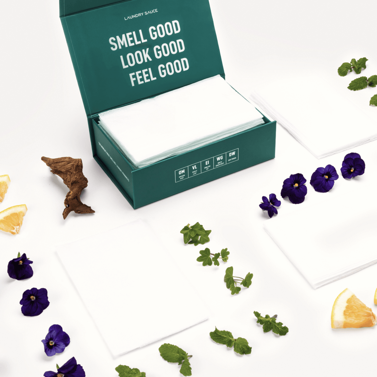 Scented dryer sheets in a teal open box with white sheets and scattered blossoms