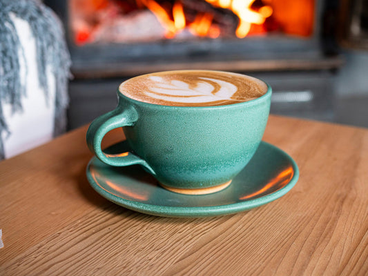 Green stoneware latte cup with curved handle and matching saucer, speckled glaze