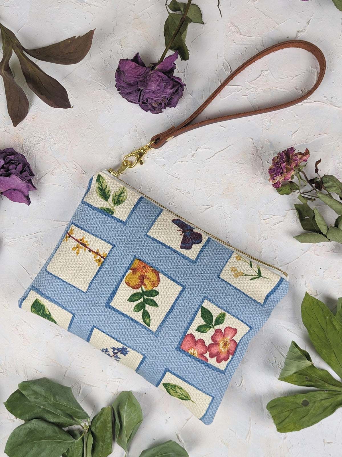 Blue patchwork wristlet purse with floral and bird print, lying flat