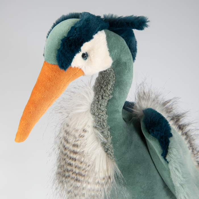 Close-up plush heron with orange beak and white face, teal head and textured feather body.