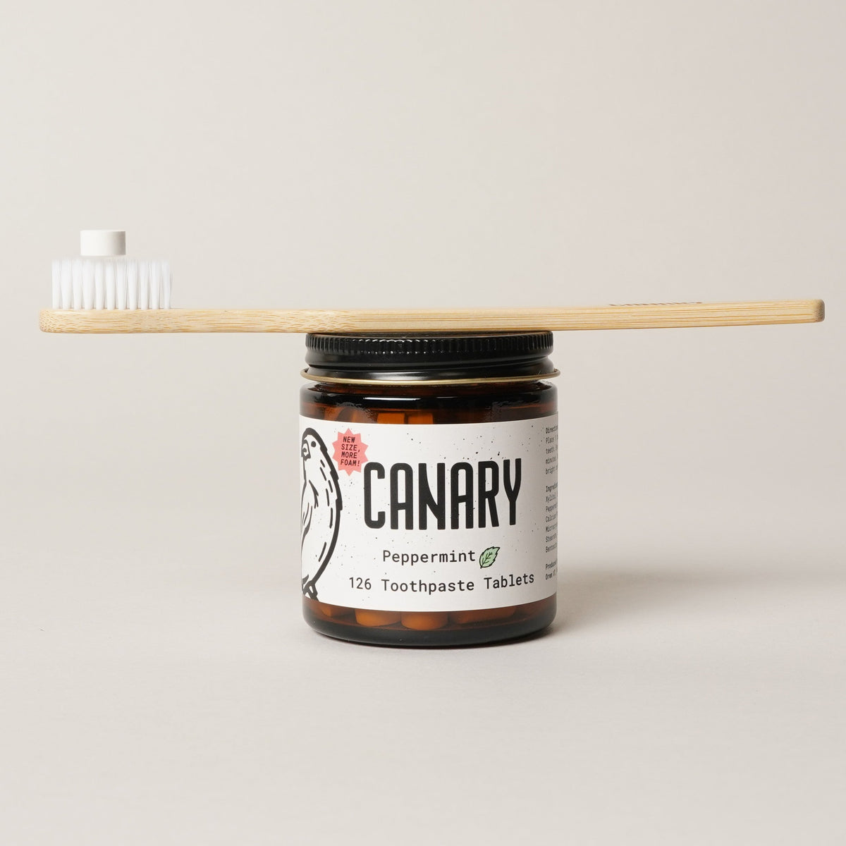 Peppermint toothpaste tablets in an amber jar beside a bamboo toothbrush