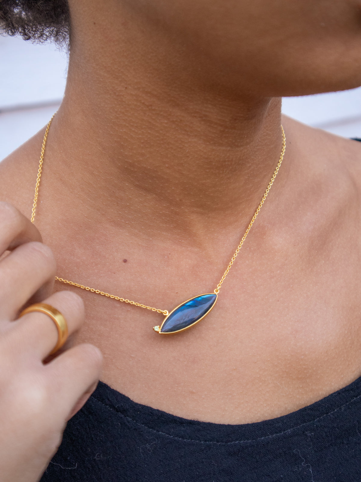 Gold chain necklace with oval blue gemstone pendant at collarbone