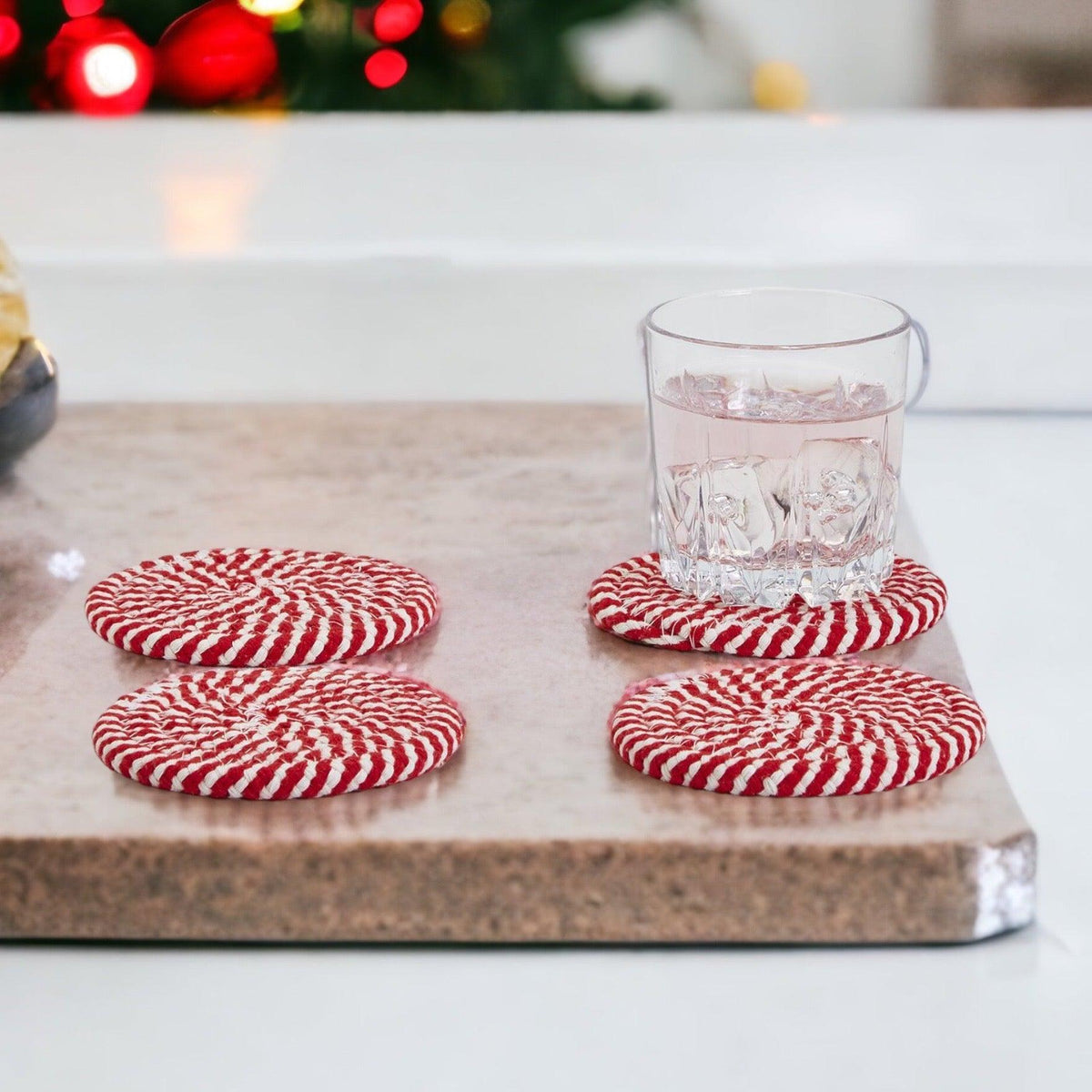 Four red and white striped braided coasters with a glass on stone