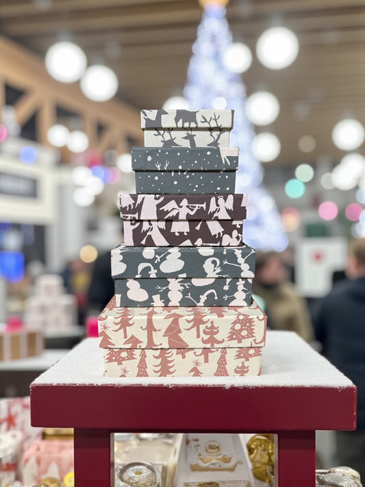 Stack of square gift boxes with gray, dark blue, and tan holiday animal and tree patterns