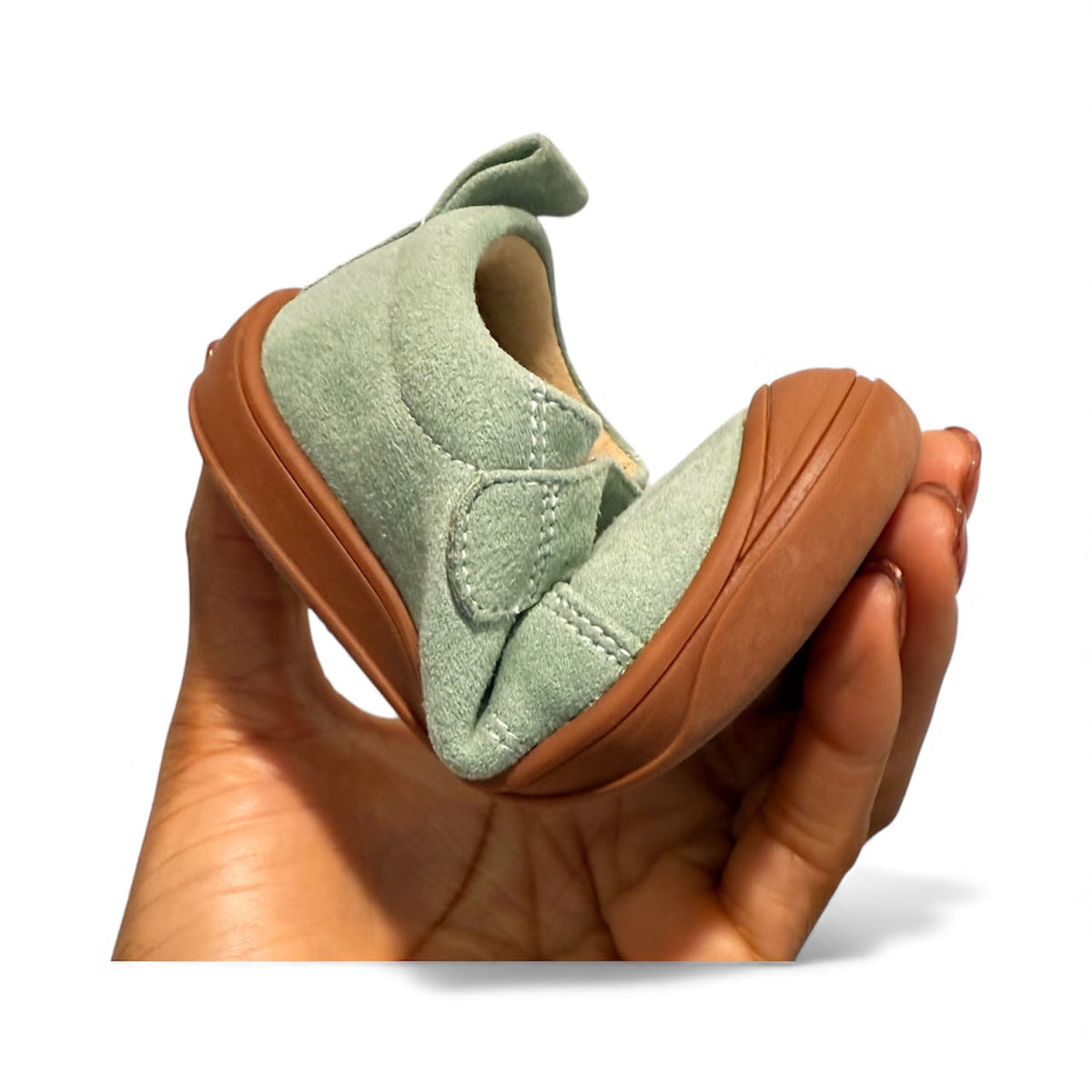 Kids’ light green barefoot sneaker held in hand, showing brown flexible rubber outsole