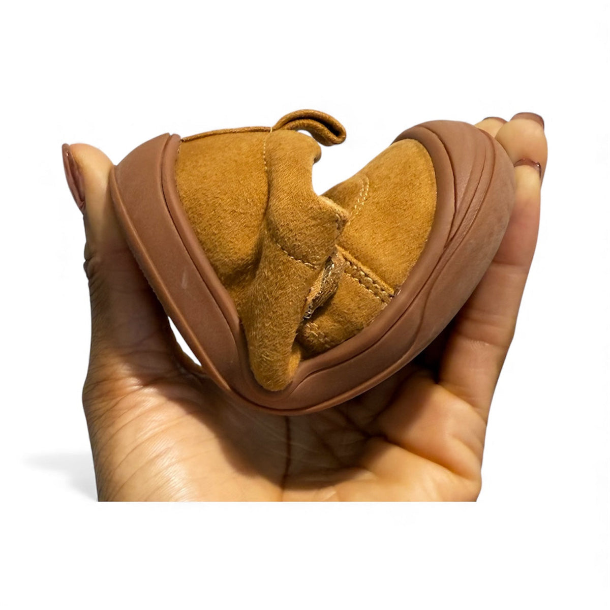 Tan suede kids' sneaker held in hand, showing rounded toe and sole
