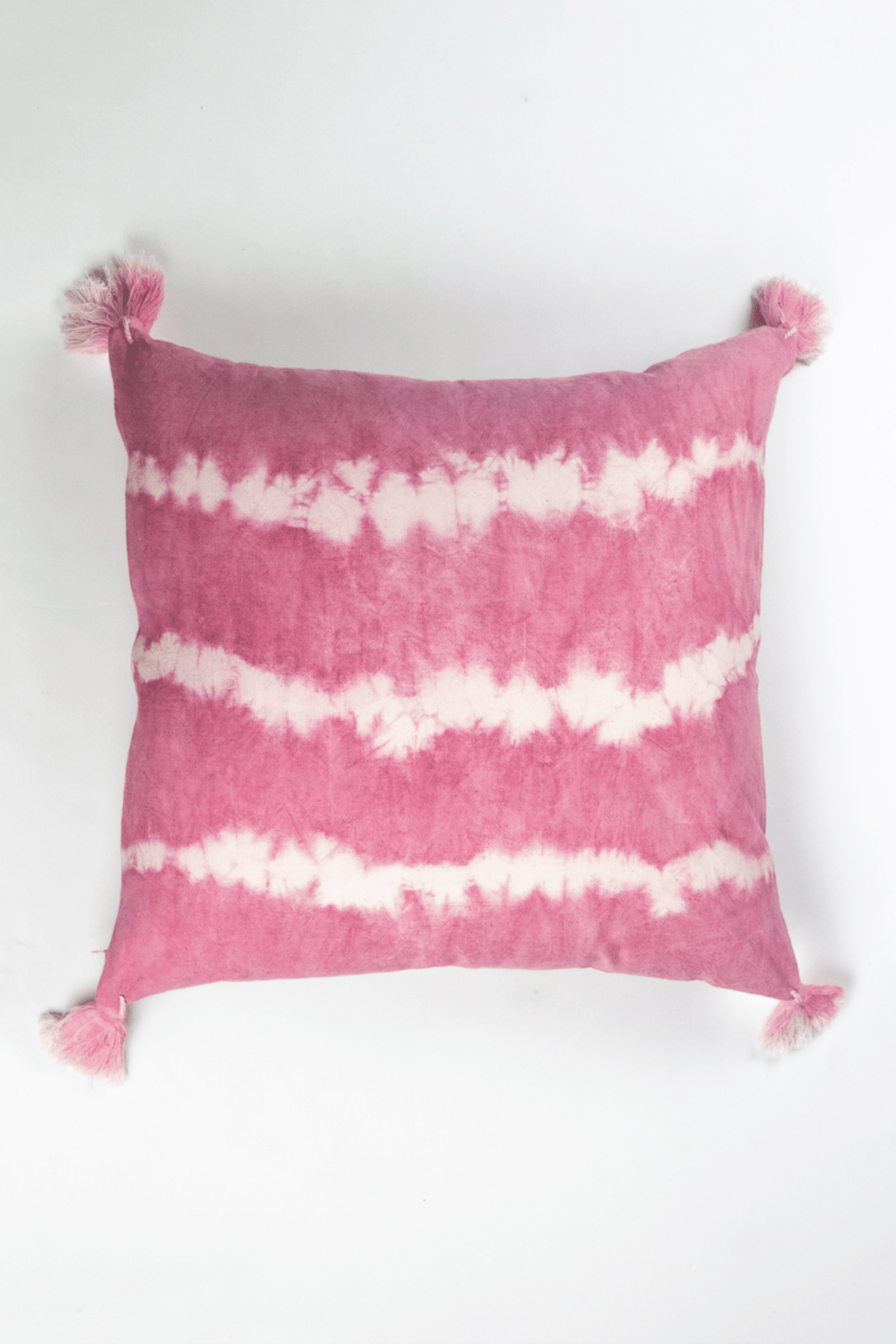 Pink shibori tie-dye square pillow with white stripe pattern and tassel fringe corners.
