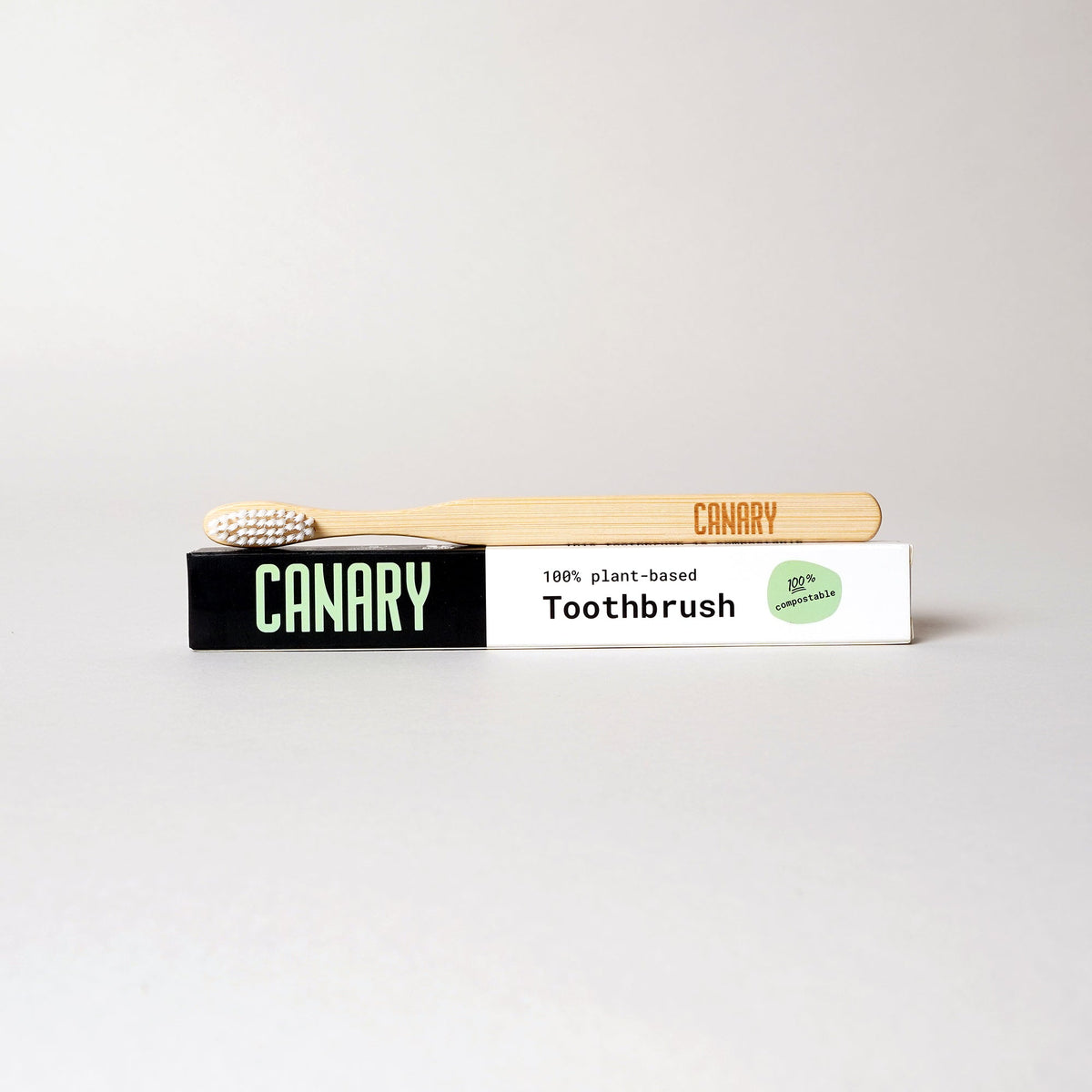 Canary bamboo toothbrush with white bristles resting on its paper box