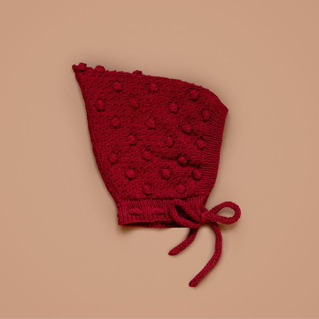 Dark red knitted pixie hat with tie strings and textured pattern