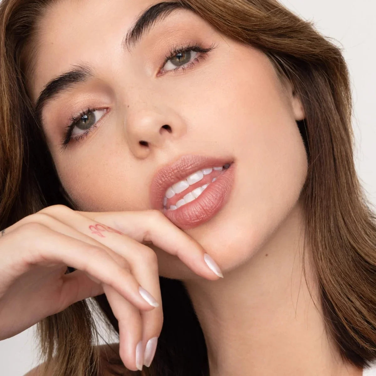 Lip tint on lips with rosy-mauve finish; hand gently touching face