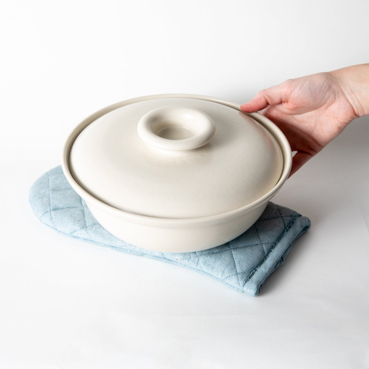 Hand placing a pot on a light blue quilted oven mitt trivet