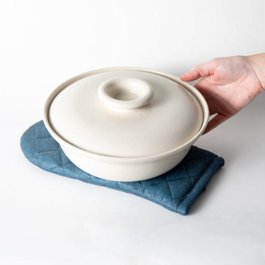 Cobalt blue quilted oven mitt trivet under a white pot, diamond stitched.