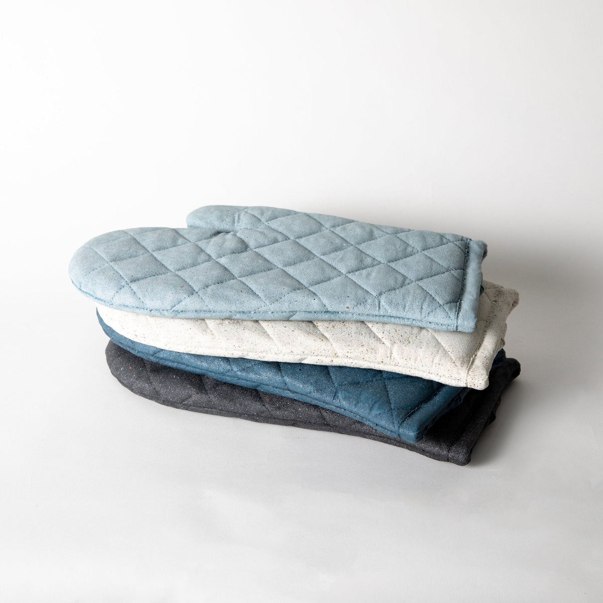 Stacked quilted oven mitt trivets in light blue, cream, and dark gray