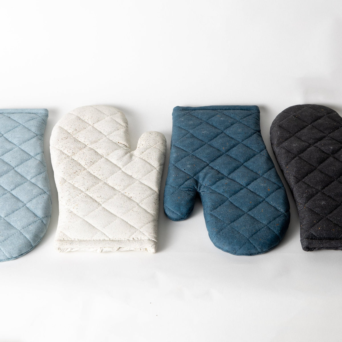 Set of quilted oven mitt trivets in light blue, cream, dark blue, and charcoal