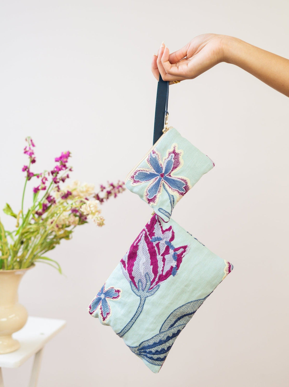 Light mint pouch with blue and purple embroidered flowers, held by strap