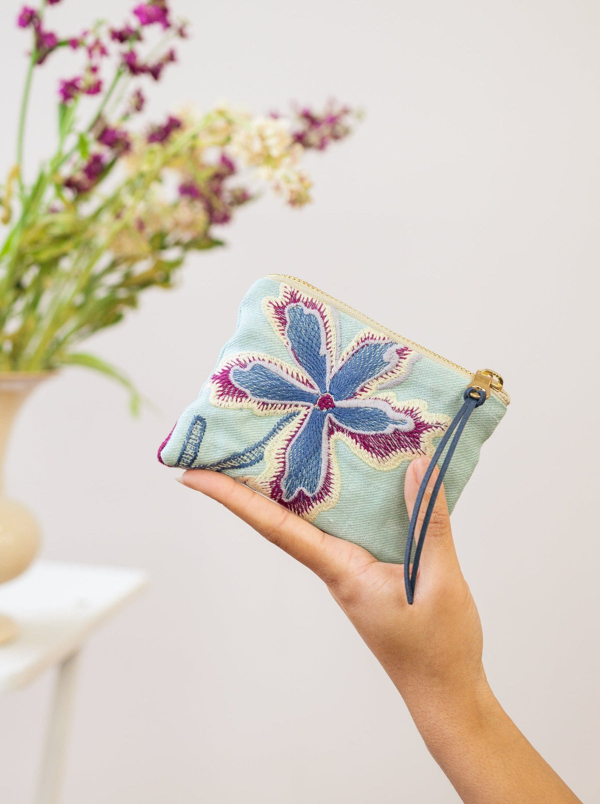 Light mint mini pouch with blue and purple floral embroidery, wrist strap visible