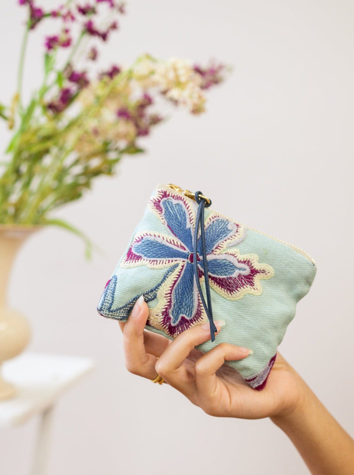Light mint pouch held in hand with blue and purple embroidered flower design