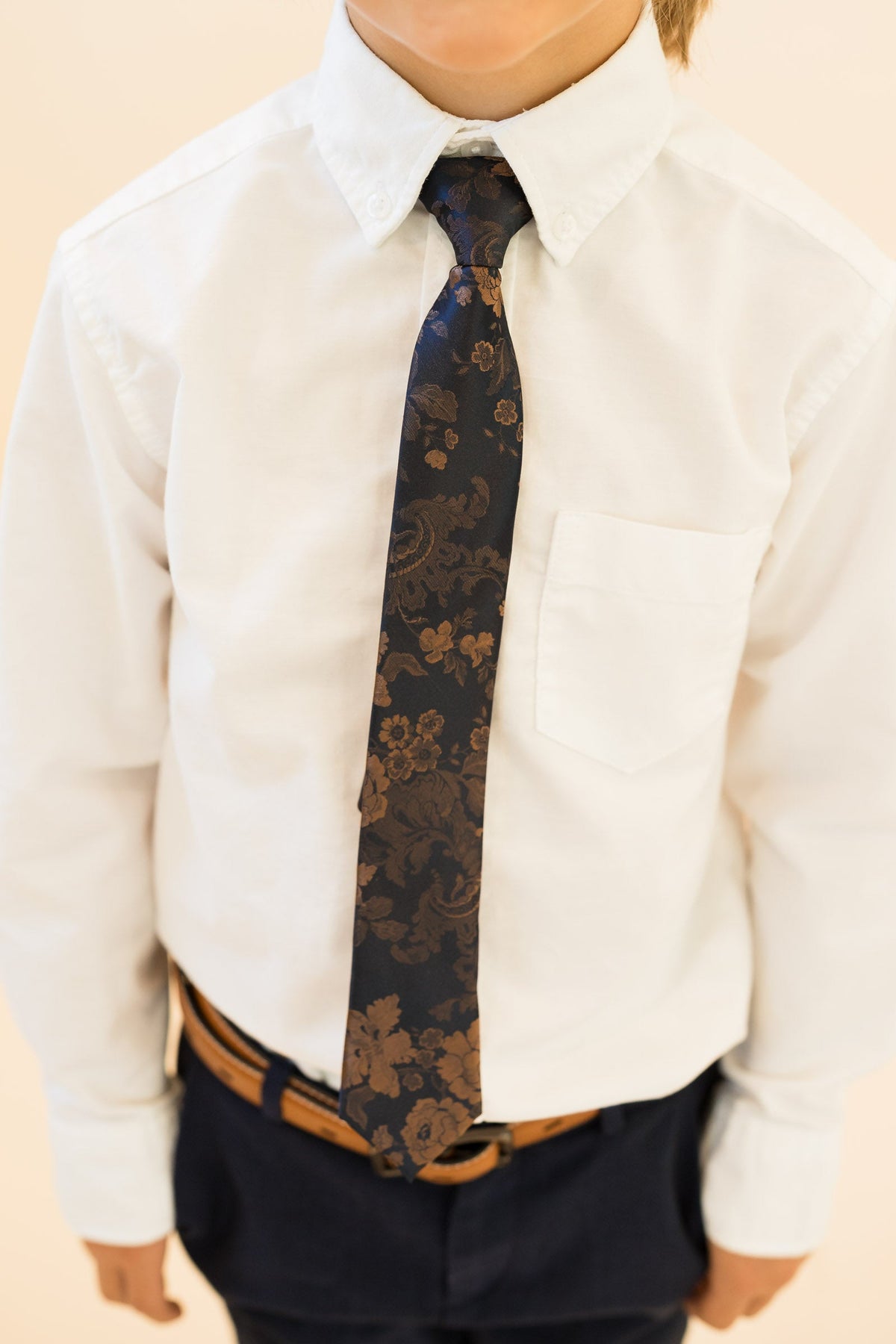 Boys necktie with dark navy and tan floral pattern, worn with white button shirt