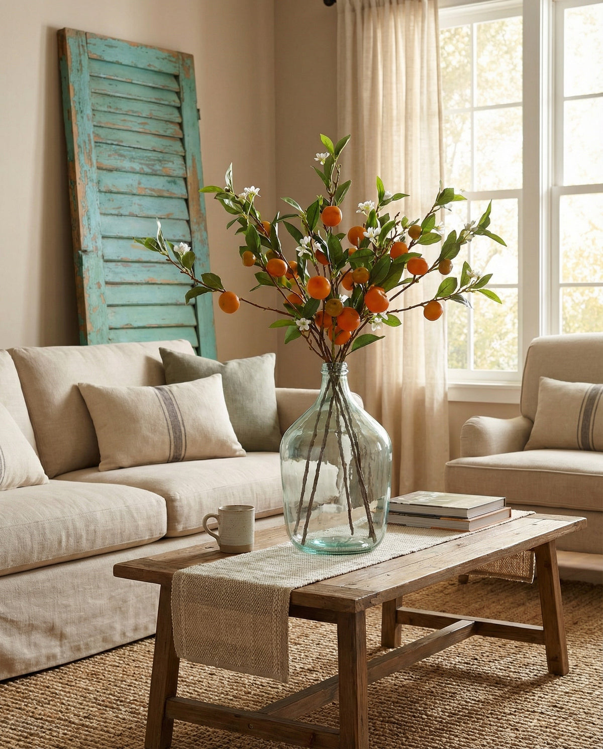 Tangerine branch stem bouquet with orange fruit and green leaves in glass vase.