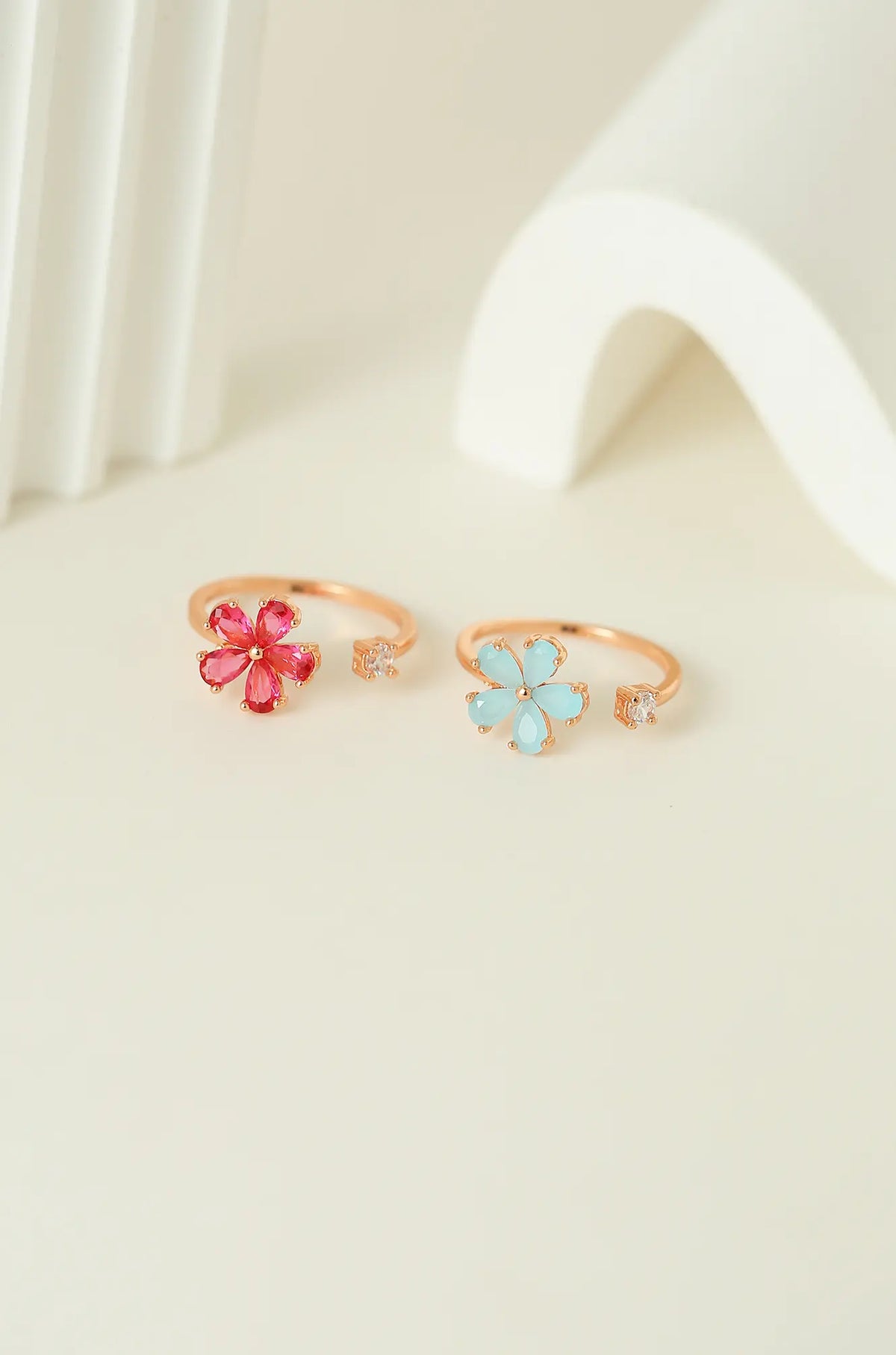 Two open gold-tone rings with red and light blue flowers and clear accent stones