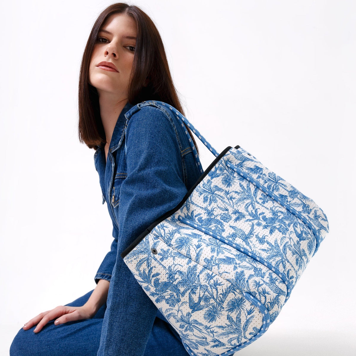 Tropical print tote with black trim and blue handles held over shoulder