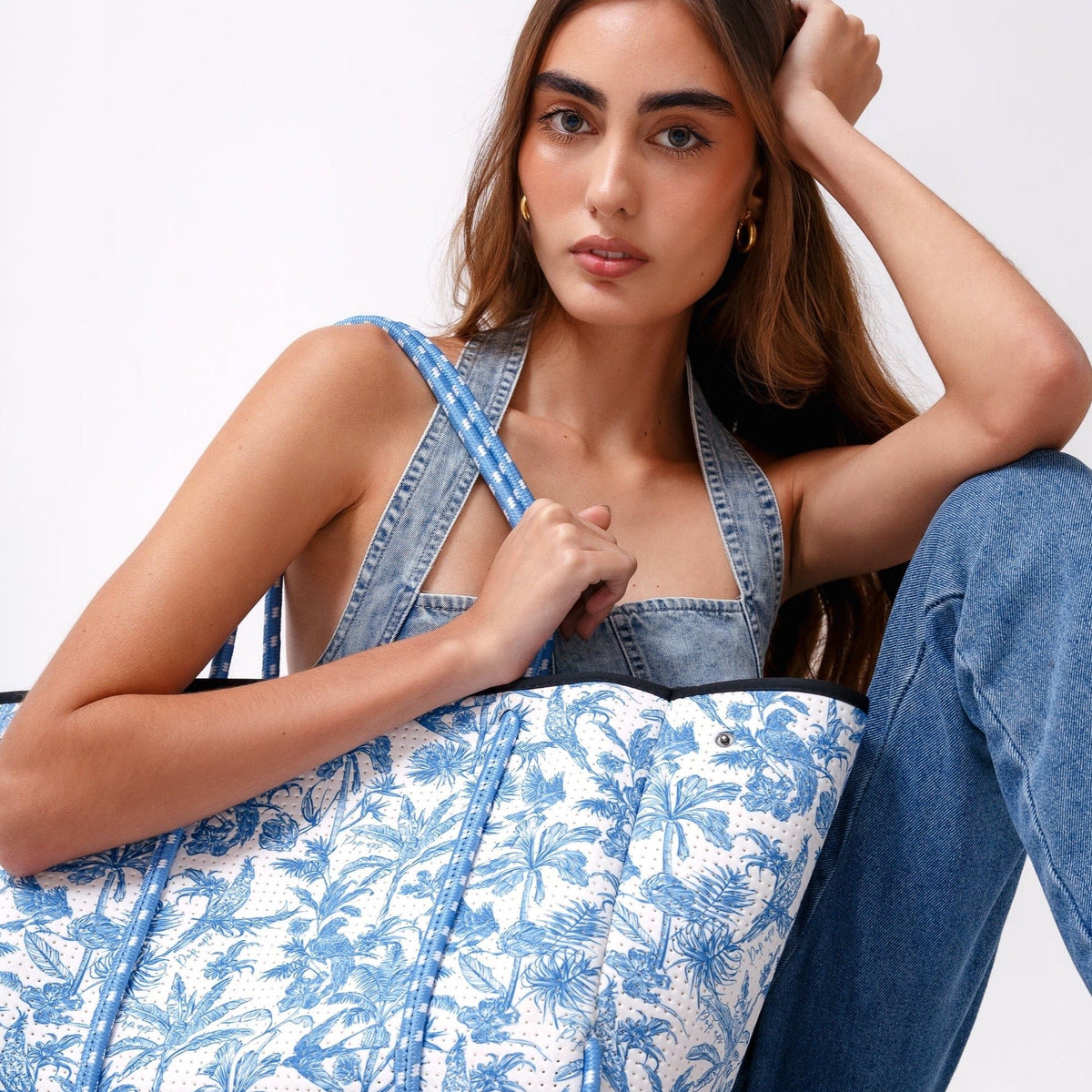 Large tote bag with blue-and-white tropical print and black top band on model