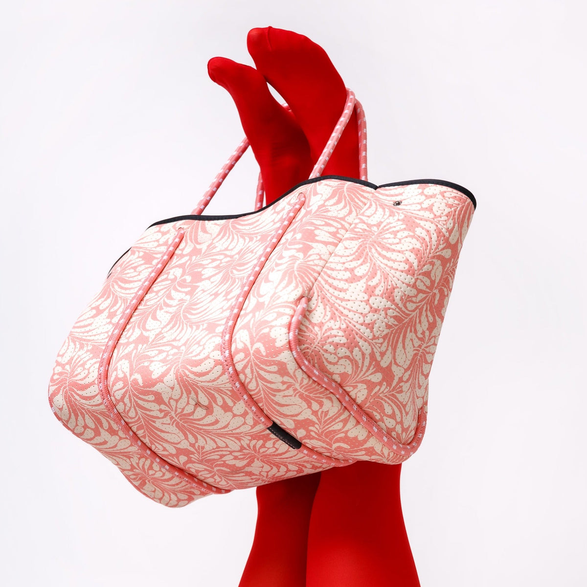 Pink palm-print tote bag with black top band and pink rope handles, angled view