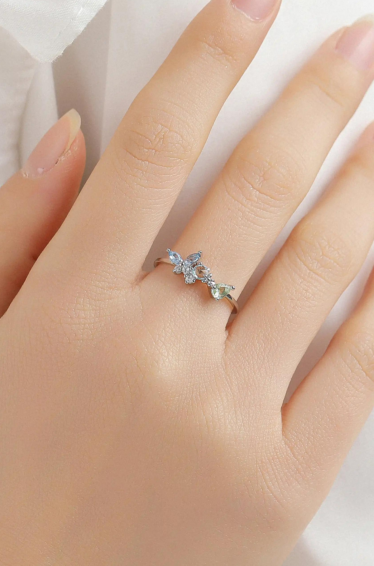 Silver butterfly ring with blue and green stones worn on a finger